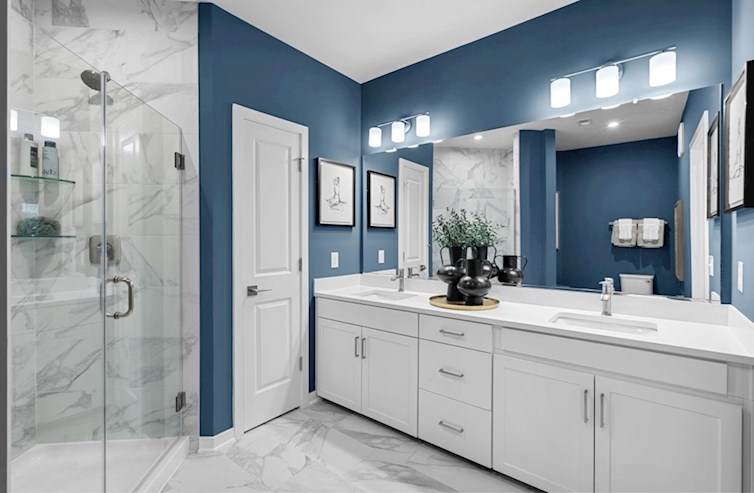 Chestnut primary bathroom with blue accent walls, walk-in shower with frameless enclosure, linen closet, artic white quartz countertops, and painted linen cabinets