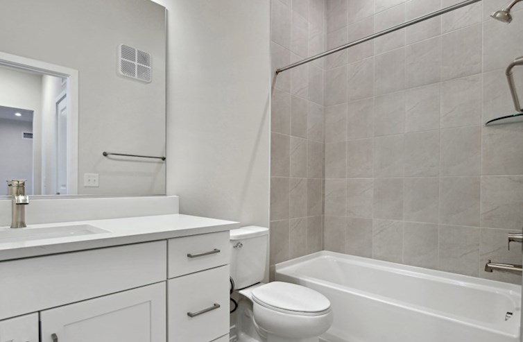 Austin secondary bathroom with a deep tub, handset ceramic wall tile, iced white quartz countertops, rectangular undermount porcelain sink, and white shaker cabinets