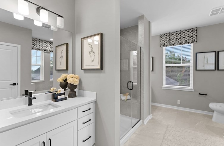 Dogwood primary bathroom with artic white countertops, white cabinets, and a large walk-in shower with a seat, handset ceramic wall tile, and a frameless enclosure