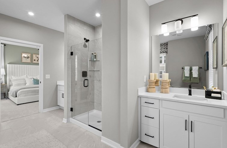 Dogwood primary bathroom with dual vanities, artic white quartz countertops, white cabinets, and a walk-in shower with a seat and frameless enclosure