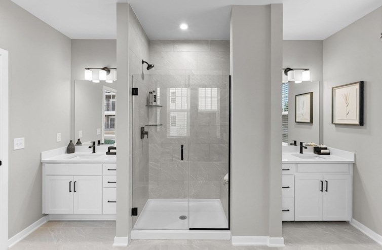 Dogwood primary bathroom with dual vanities, artic white quartz countertops, white cabinets, and a walk-in shower with a seat and frameless enclosure