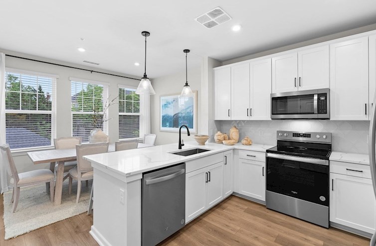 Dogwood eat-in kitchen with 3 windows, 2 pendant lights, white cabinets, calacatta classique quartz countertops, stainless steel appliances, and black hardware overlooking the breakfast area